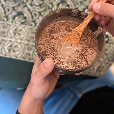 Hand holding a coconut bowl with chocolate liquid, with chocolate sprinkles on top.