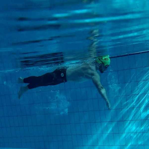 Underwater photo of man swimming in a green cap and full length neoprene trousers.