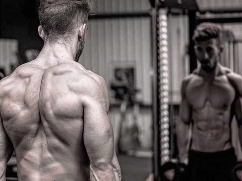 Black and white image of ripped man standing in front of the mirror.