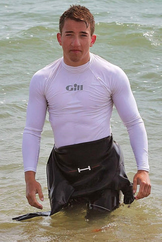 Man in the sea, wearing a rash vest with a wetsuit around pulled up to his waist.