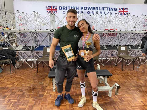 Women holding weightlifting trophy next to a man.